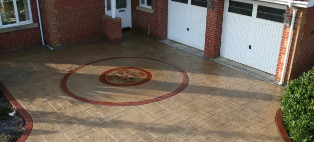 Pattern imprinted concrete driveway by PICS, featuring custom circular design in front of garage.